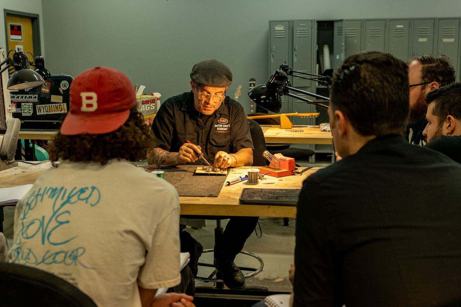 Guitar luthier working on pickups while students observe in class